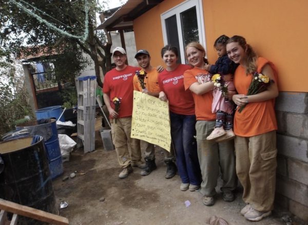 Pictured is a building group, a member of the family that will be living in the house, and the house built.
